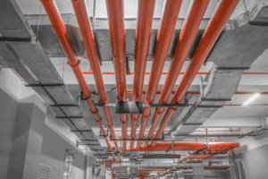Overhead fire sprinkler piping network with red pipes installed in a commercial building, illustrating NFPA 13, 13R, and 13D system design differences