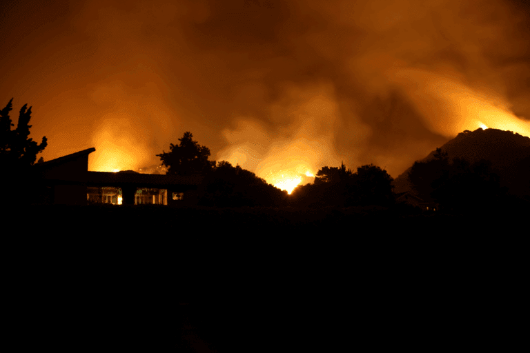 Wildfire burning along a hillside at night near homes in the wildland urban interface