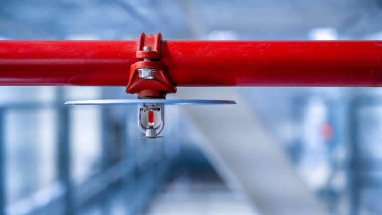 Close-up of a fire sprinkler head attached to a red fire protection pipe in a commercial building